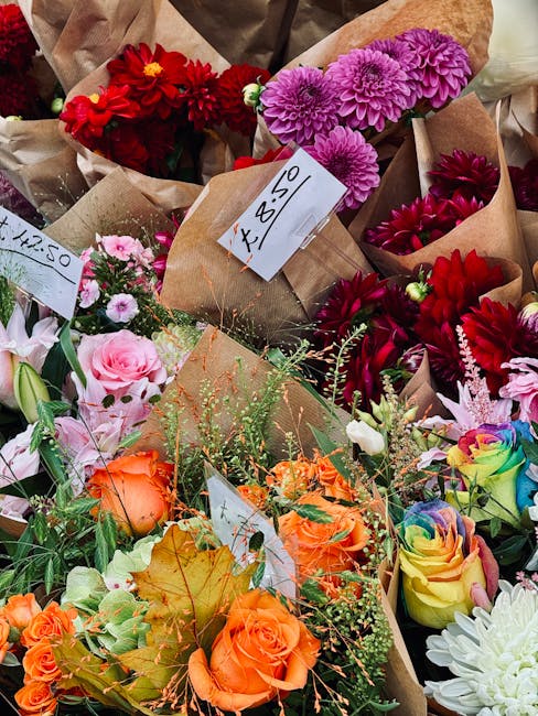 A vibrant assortment of fresh flower bouquets displayed closely together, featuring a variety of blooms including deep red dahlias, bright pink dahlias, orange roses, pale pink roses, and multicolored