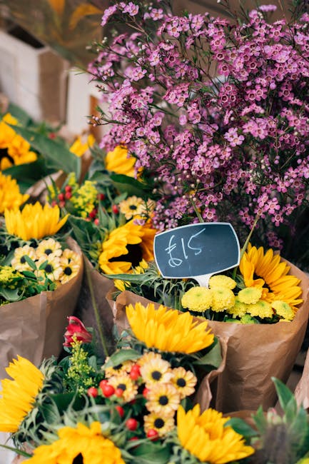 A vibrant display of fresh floral arrangements at a flower market, featuring a variety of colorful blooms including bright yellow sunflowers with large petals and green centers, smaller daisy-like flo